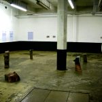 wide view of exhibition space showing letters on the wall, logs on the floor and evidence bags hanging from the ceiling