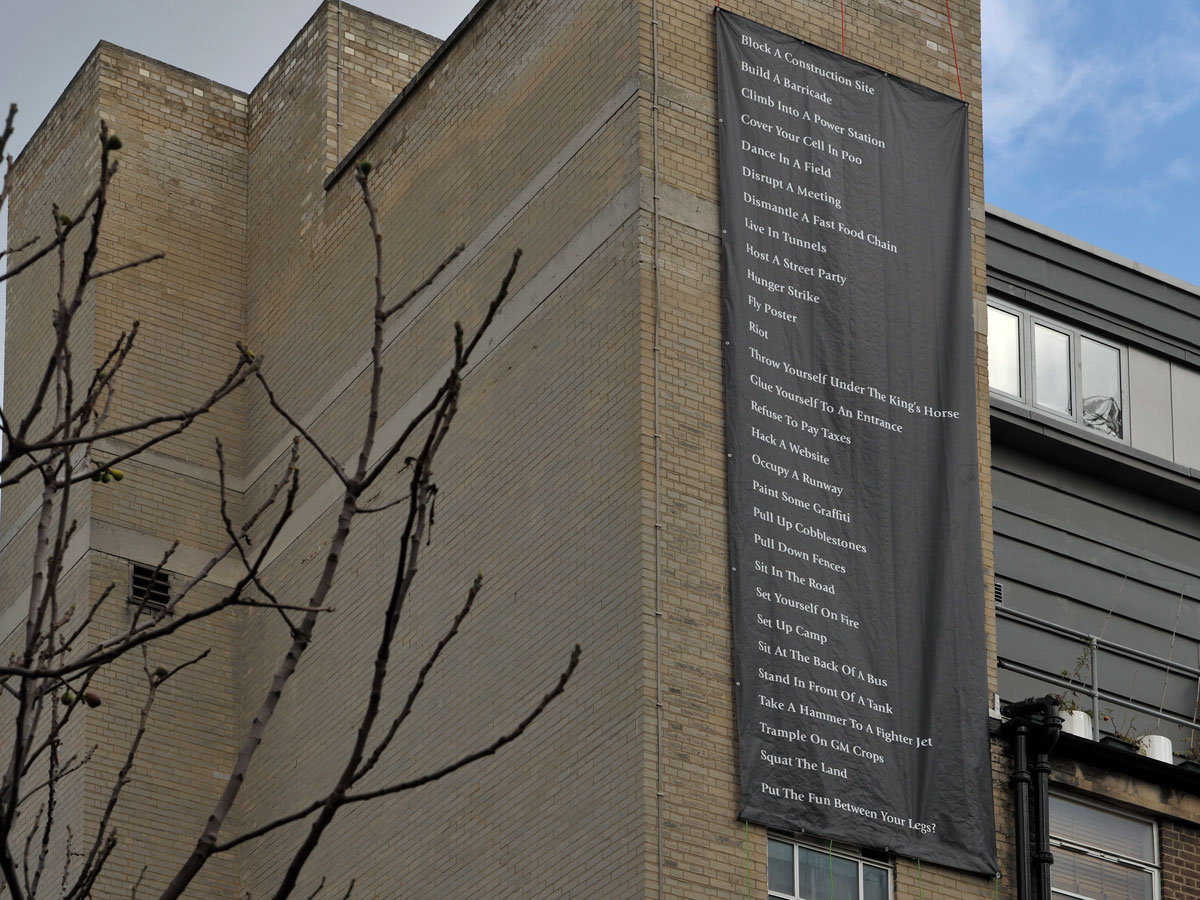 a large black banner hanging on a tall brick building displaying a list civil disobedience forms