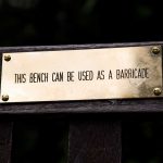 close up of a copper bench plaque that says "this bench can be used as a barricade"