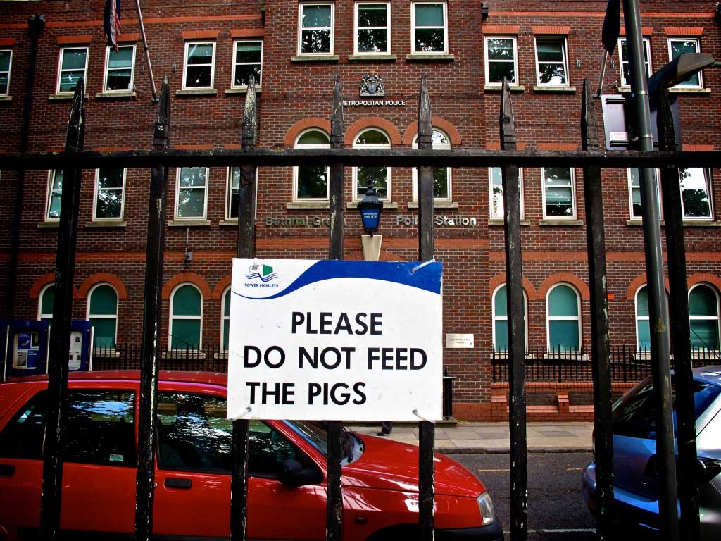 Towera sign on railings opposite a police station altered to read 'Please Do Not Feed the Pigs'
