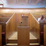 looking out from a lectern in a lecture hall a man sits on the right with his head in his hands