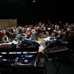 an audience sitting in a darkened room with dj and sound equipment
