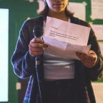 Cropped image of a young person holding a piece of paper and a microphone.