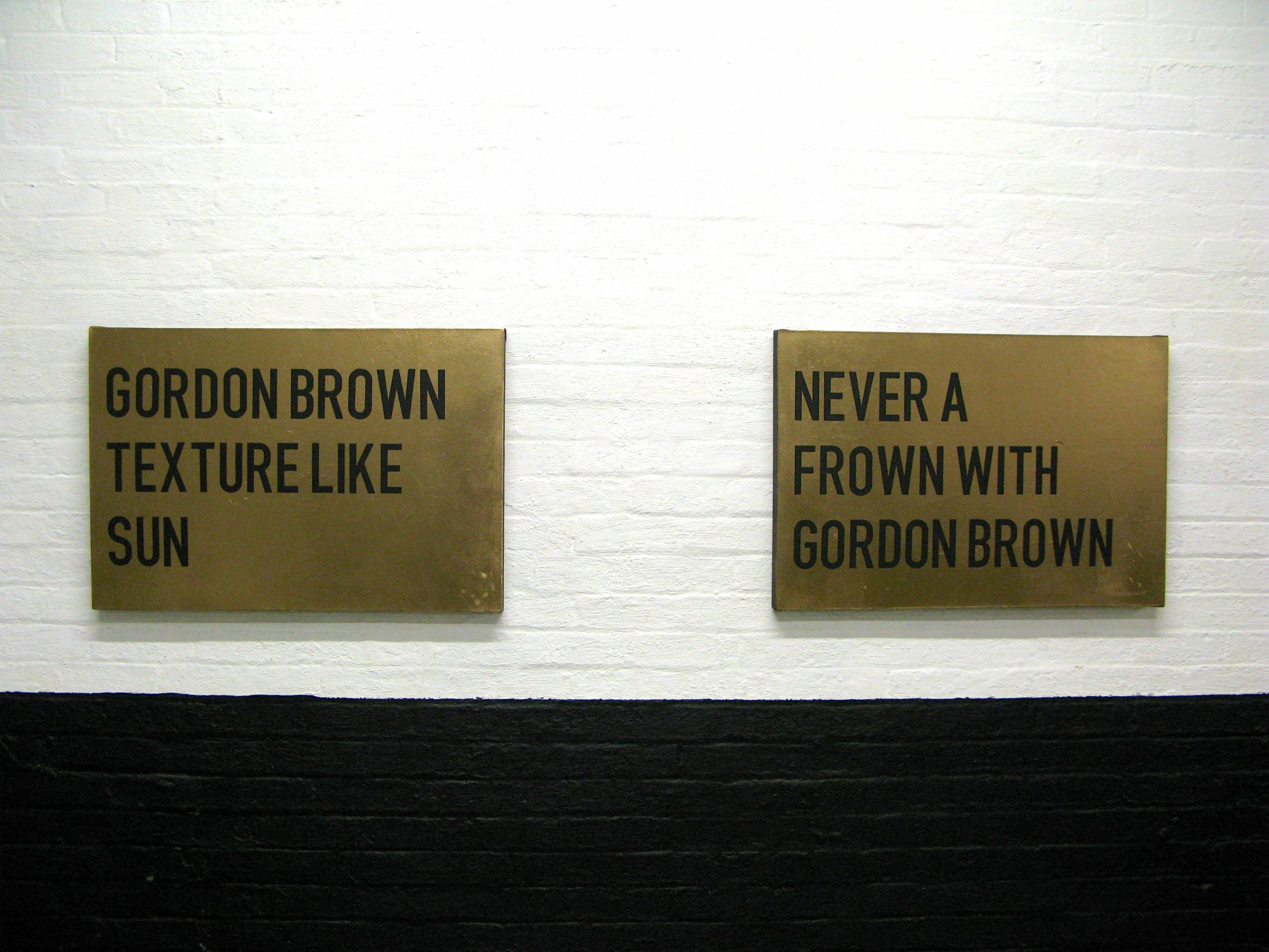 two gold paintings with black text, one reads "Gordon Brown texture like sun" the other "never a frown with Gordon Brown"