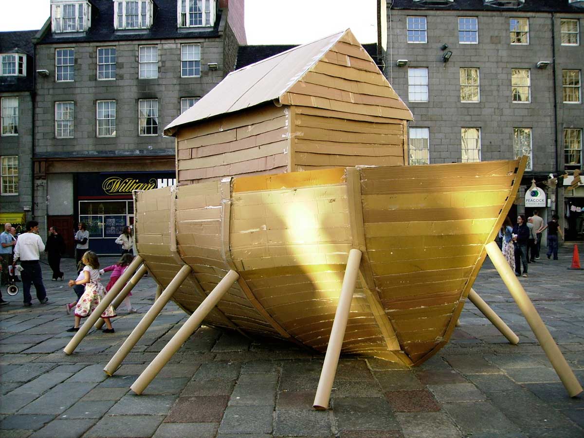 a boat made of cardboard outside on a paved area in front of some shops
