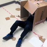 Childs legs sticking out of a large cardboard box on the floor surrounded by art materials