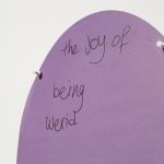 "The joy of being weird" written in black pen on purple paper.