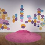 Image showing the gallery wall, which is white with clusters of colourful egg/ellipse shapes stuck onto it. A large pink circle is stuck to the floor and creeps up the wall.