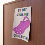 Photograph of a hand-drawn A4-sized poster which is taped to a wood background. The drawing is of a pink croc shoe with the text "I'm not gonna hit croc bottom" written in colourful letters.